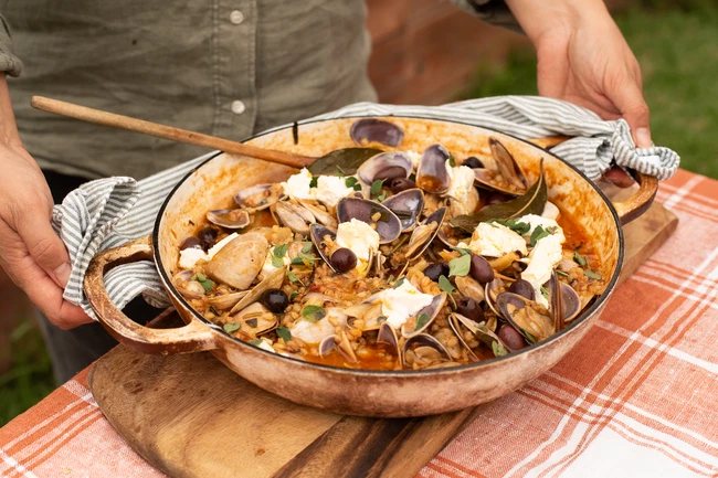 A pan of clams, olives and white beans, held outdoors